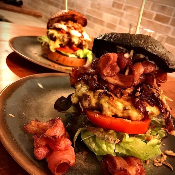Hamburguesa alta con bacon crujiente y salsa, servida en plato de piedra.