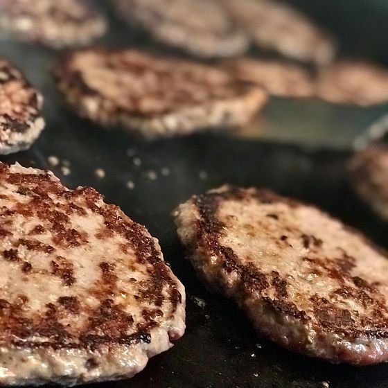Dos hamburguesas de carne marcándose sobre la parrilla caliente de piedra volcánica.