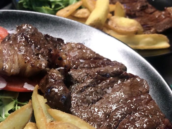 Entrecote a la parrilla con patatas gajo, rúcula y tomate en plato de piedra.