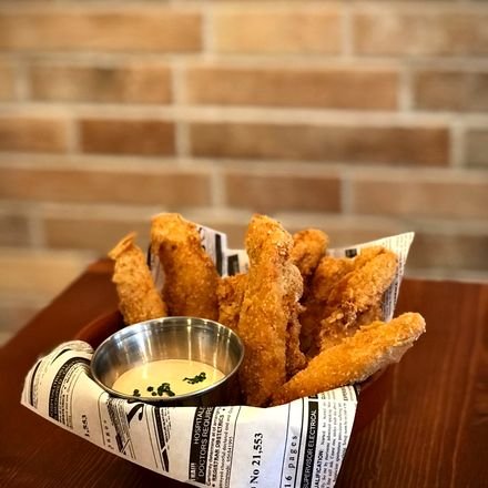 Crispy chicken fingers servidos en cucurucho de papel con salsa aparte.