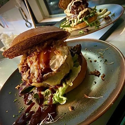 Hamburguesa alta con cebolla caramelizada y salsa de trufa sobre plato de piedra.